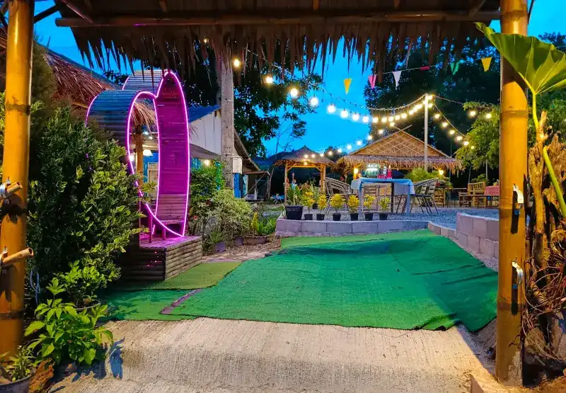 The garden entrance at dusk, with string lights, thatched salas and a neon heart