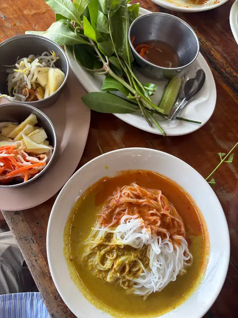 A plate of khanom jeen in curry with bean sprouts, carrot and herbs