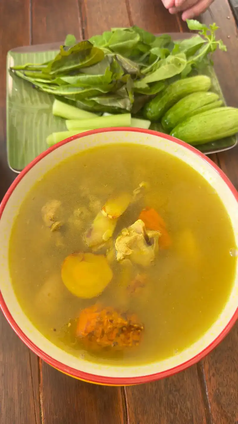 A bowl of yellow curry soup with fresh greens and cucumber on the side