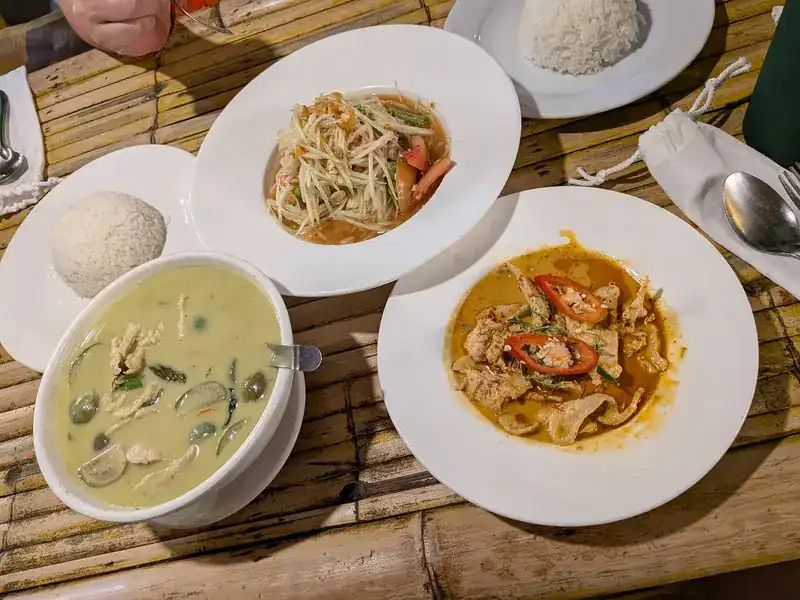Green curry, papaya salad and a red curry with rice on a bamboo table
