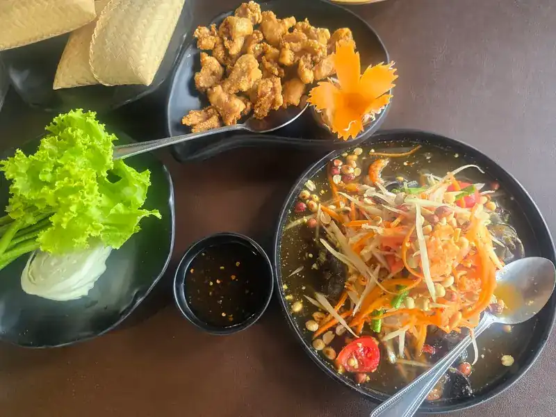 Papaya salad with fresh greens, a dipping sauce and sticky rice in a woven basket