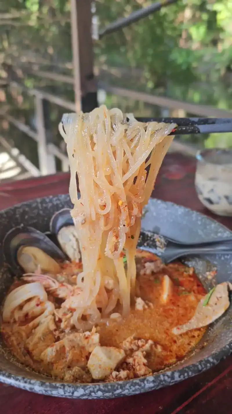 Chopsticks lifting noodles from a seafood tom yum with mussels