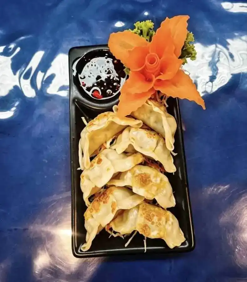 Pan-fried gyoza with dipping sauce and a carved carrot flower