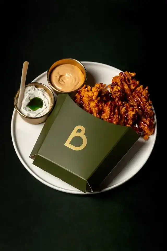 Fried chicken in a green paper sleeve with two dips