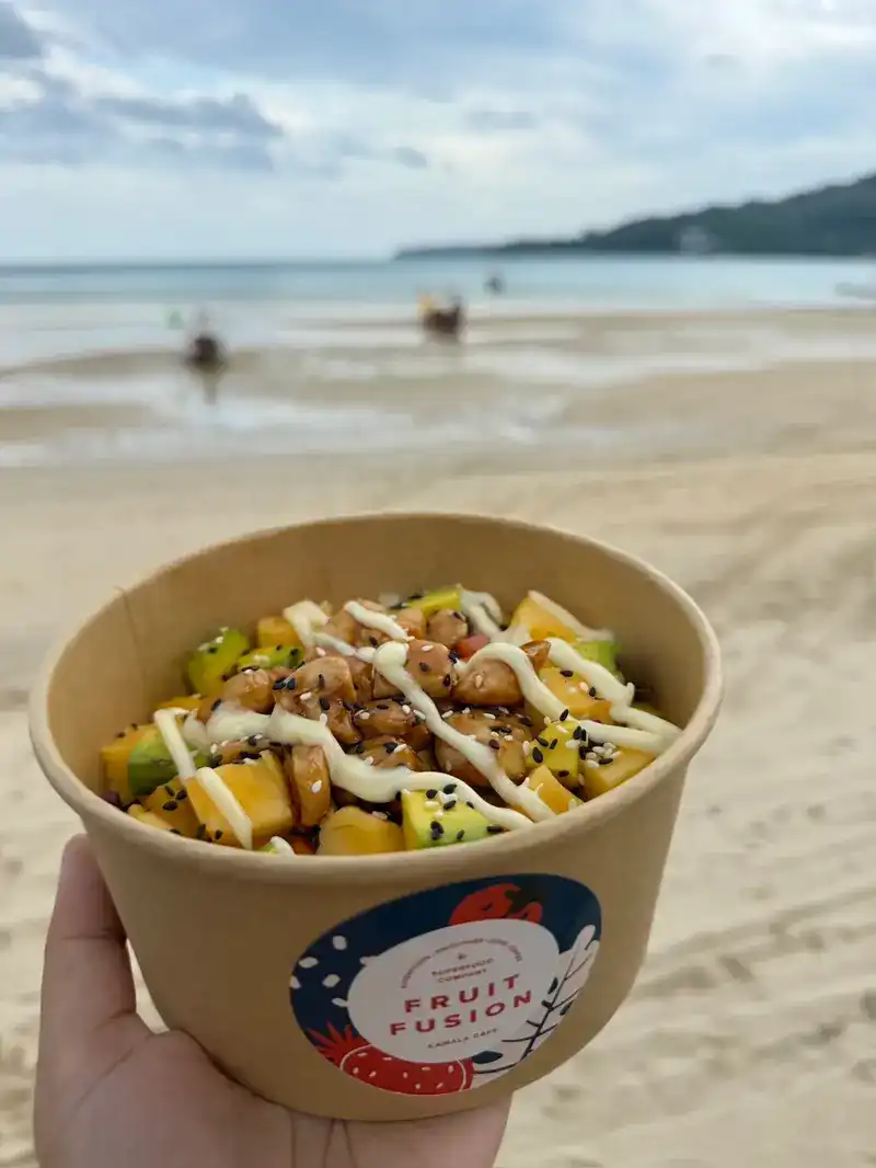 A Fruit Fusion poke bowl with mango, avocado and sesame, held up on a beach