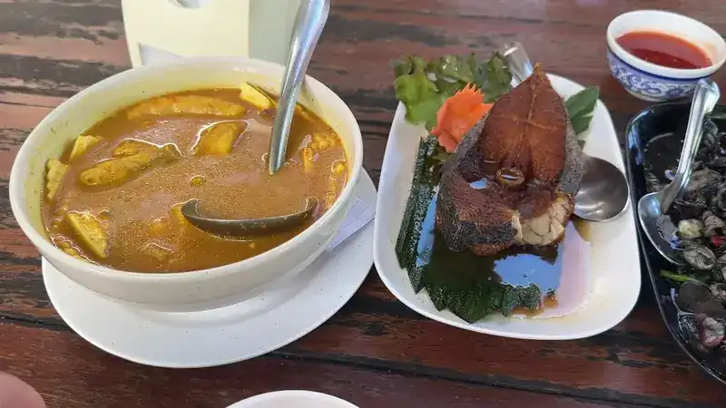 A yellow curry, fried fish and a plate of shellfish on a wooden table