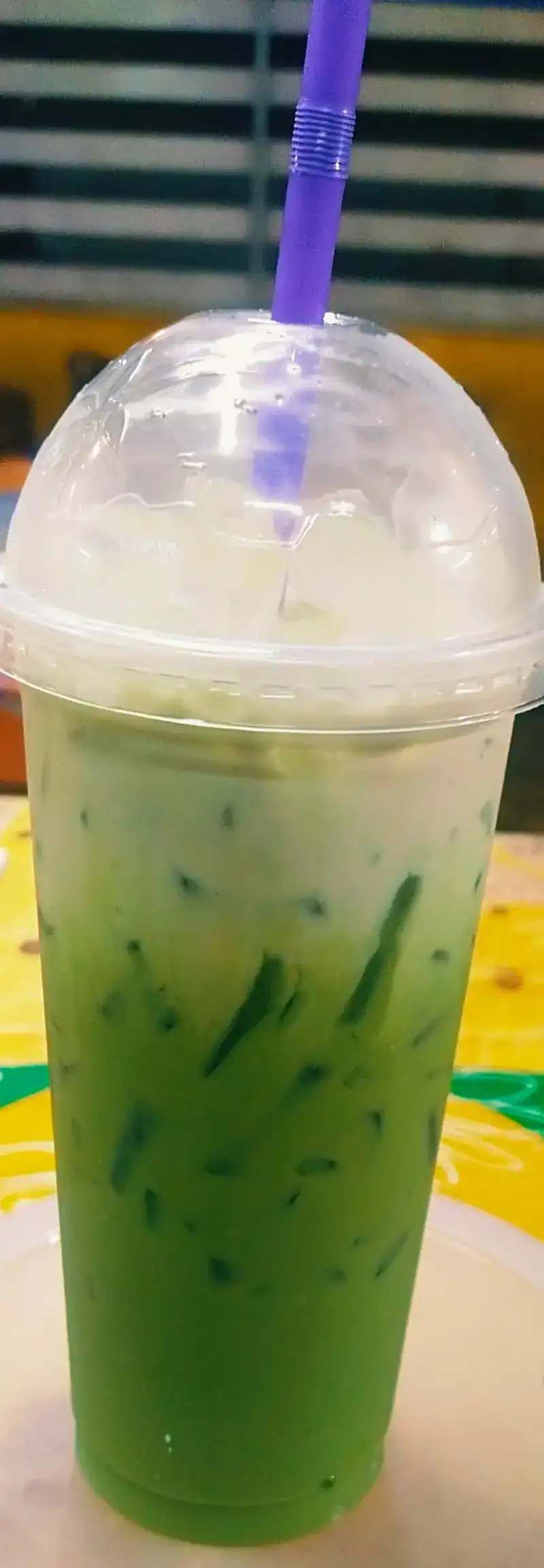 A tall iced green tea with milk in a takeaway cup