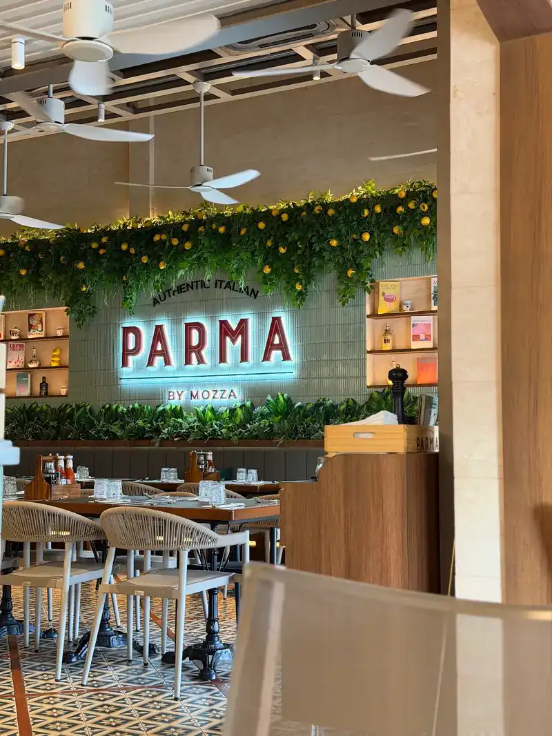 The dining room: the lit Parma sign on a green tiled wall under a garland of leaves and lemons
