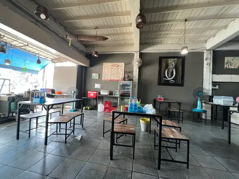 Inside the shop: steel tables with wooden benches, fans and woven basket lamps under a white ceiling