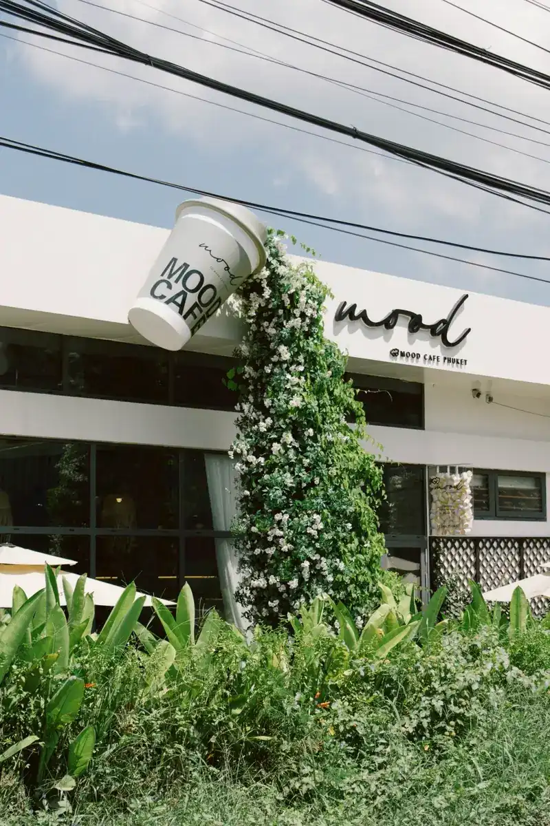 The white front of Moodcafé with a big cup on the wall and a column of climbing flowers