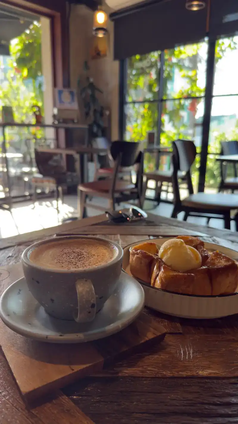A hot drink and a pastry on a wooden board by the window