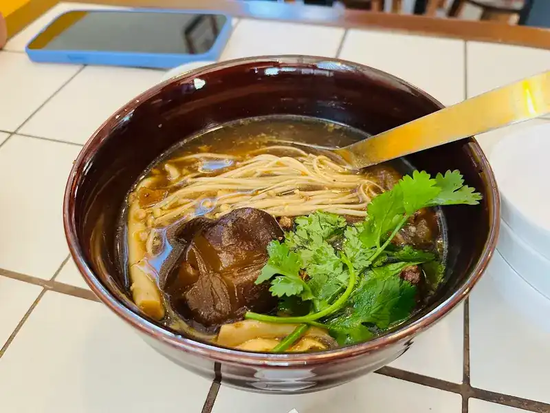 A bowl of noodle soup with a braised topping and fresh coriander