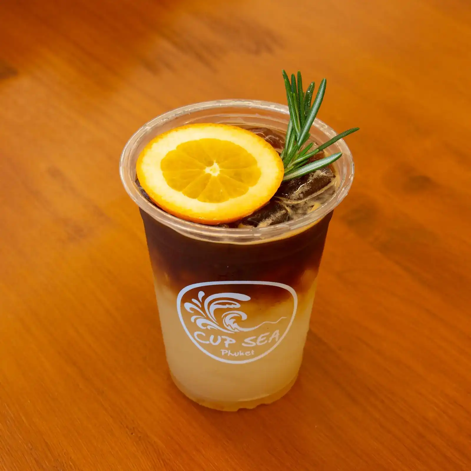 Iced orange coffee in a CUP SEA cup, with an orange slice and rosemary, on a wooden table