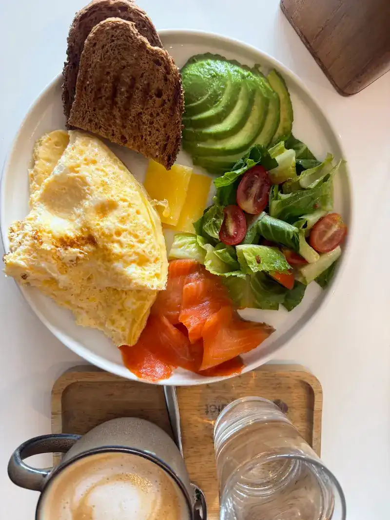Seen from above: omelette, salmon, avocado, salad and toast on one plate, with a cappuccino