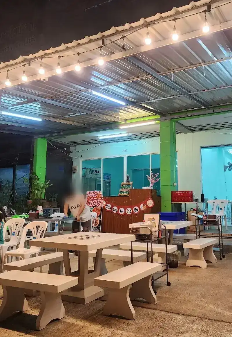 The open-air tables at night under a tin roof and a row of bulbs, with the green-pillared shopfront behind
