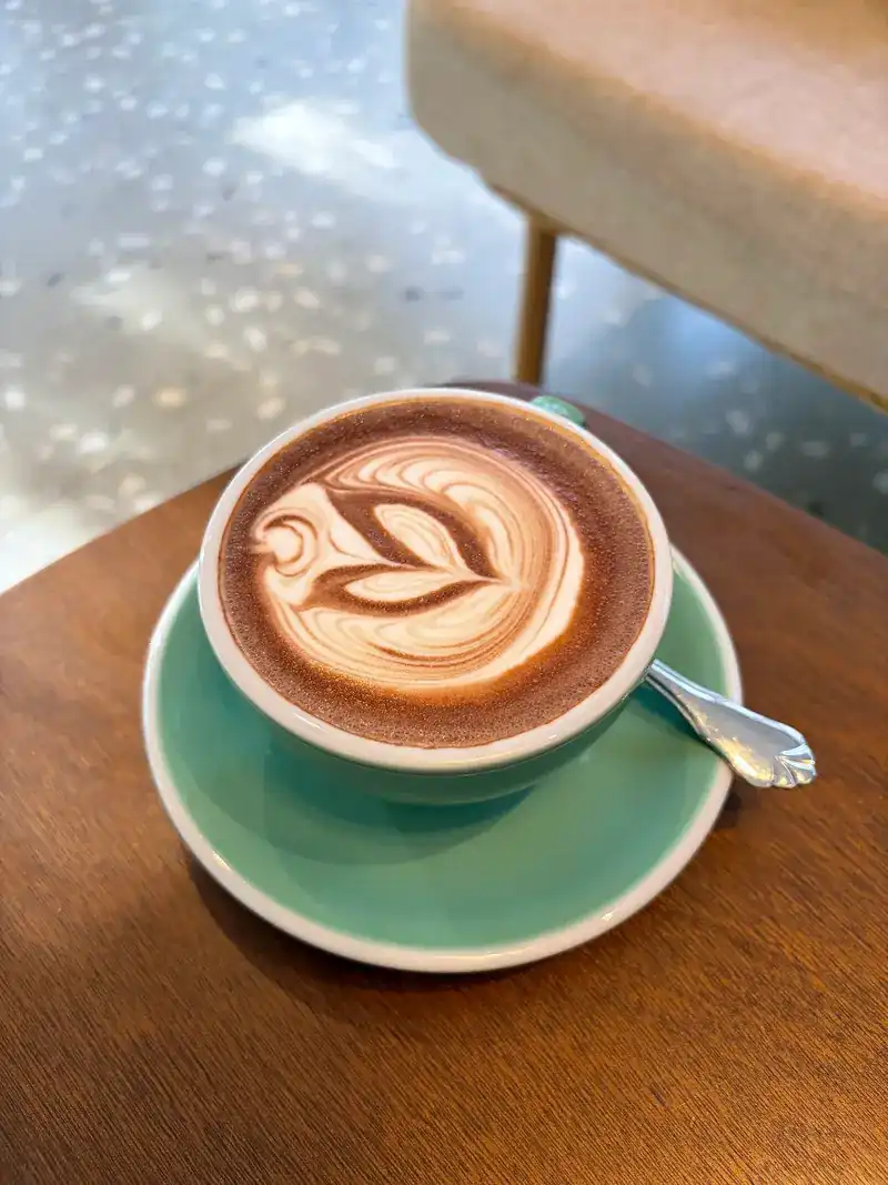 A hot latte with leaf latte art in a green cup and saucer