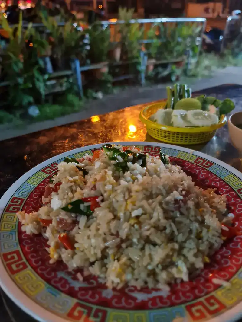 Fried rice at a table out front at night, with a basket of cucumber, lime and long beans