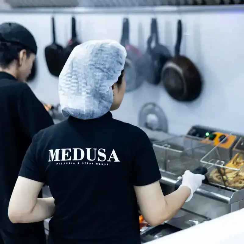 A cook in a Medusa shirt at the fryer, seen from behind