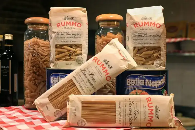 Packs and jars of dried pasta and tins of tomatoes on a checked tablecloth