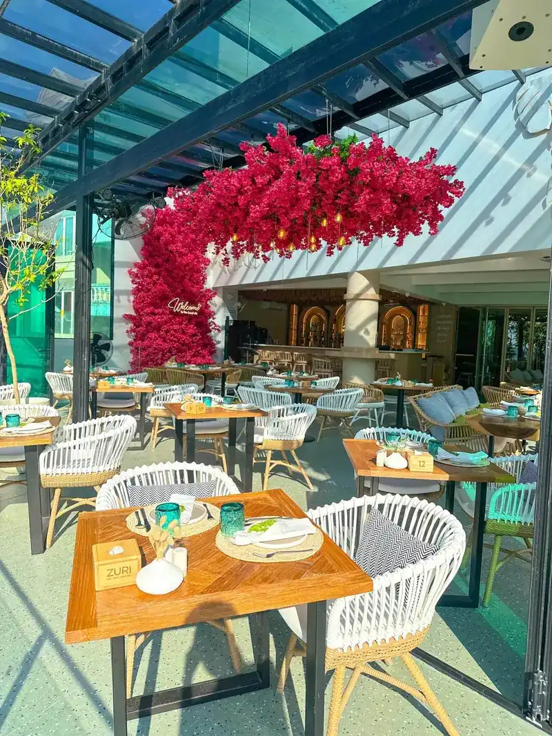 Terrace tables set with turquoise glasses under an arch of red bougainvillea