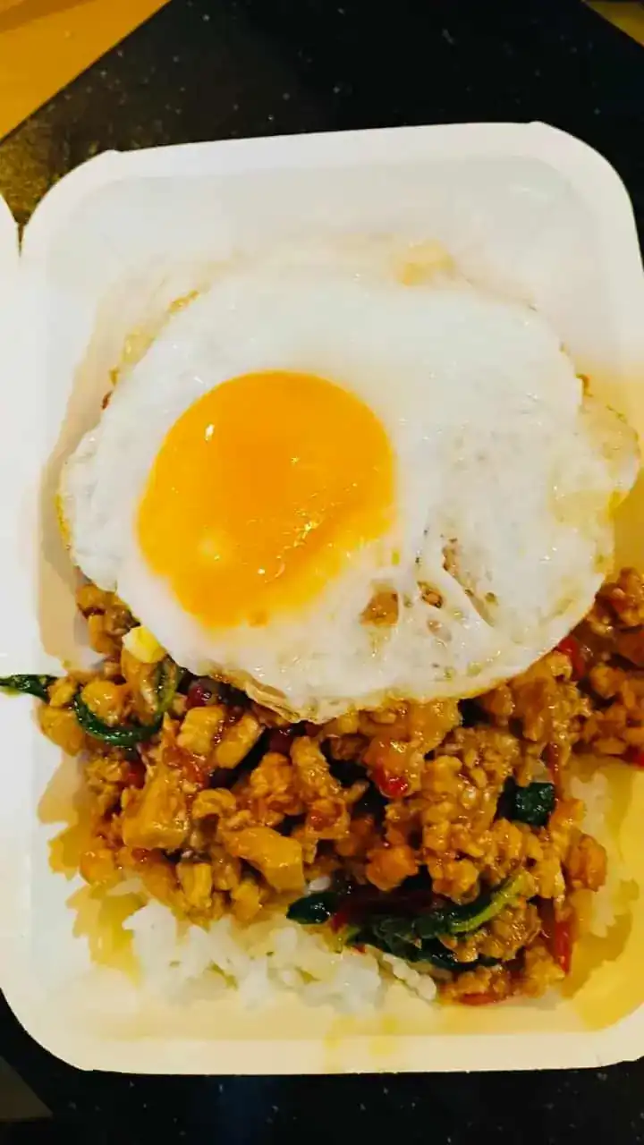 Stir-fried holy basil with minced meat on rice, topped with a fried egg, in a takeaway box