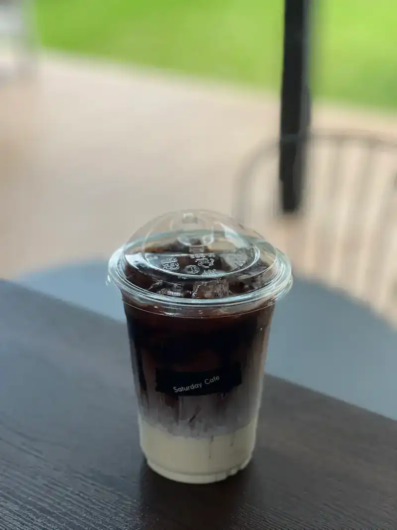 An iced coffee layered over milk in a Saturday Cafe cup