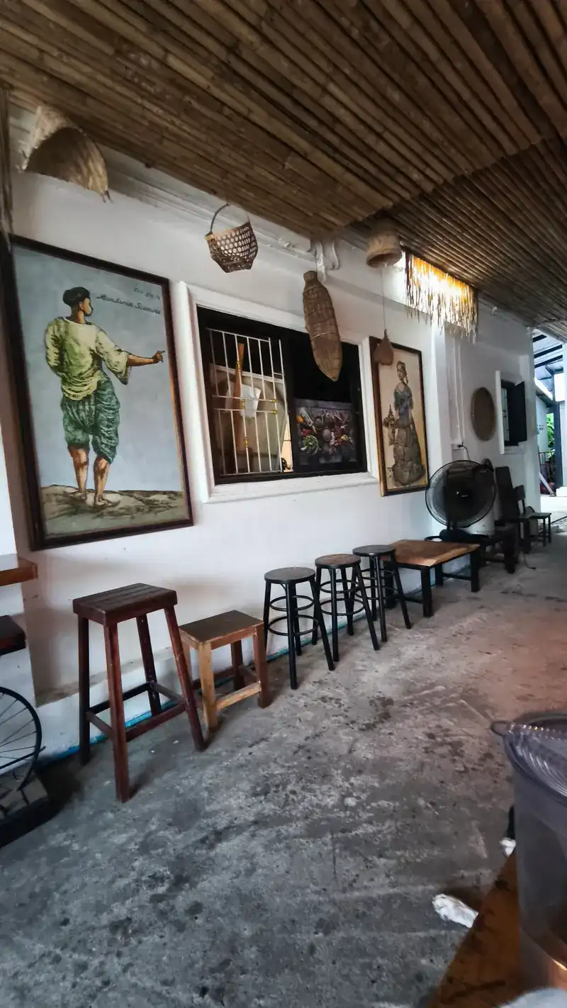 A white wall hung with paintings, wooden stools below