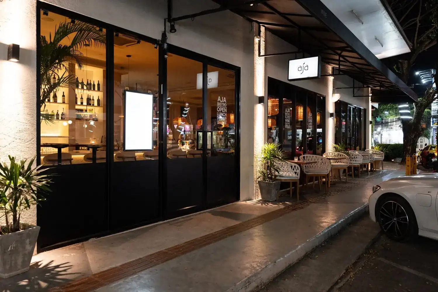 The glass front of Aja Bistro & Bar lit up at night on Boat Avenue