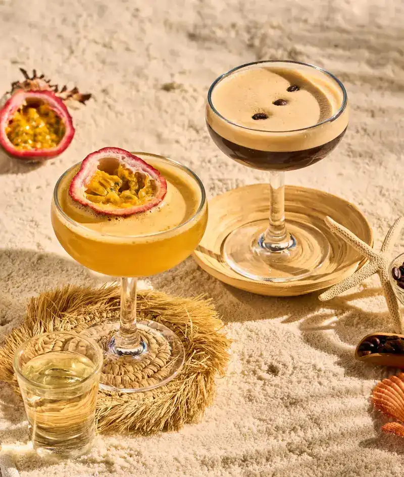 Two cocktails in coupe glasses on the sand