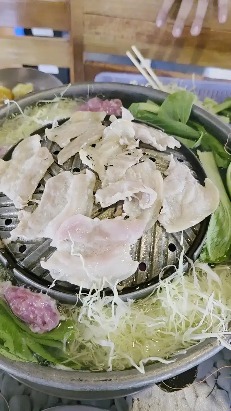 Thin slices of pork on the dome of a mookata pan, vegetables in the broth around it