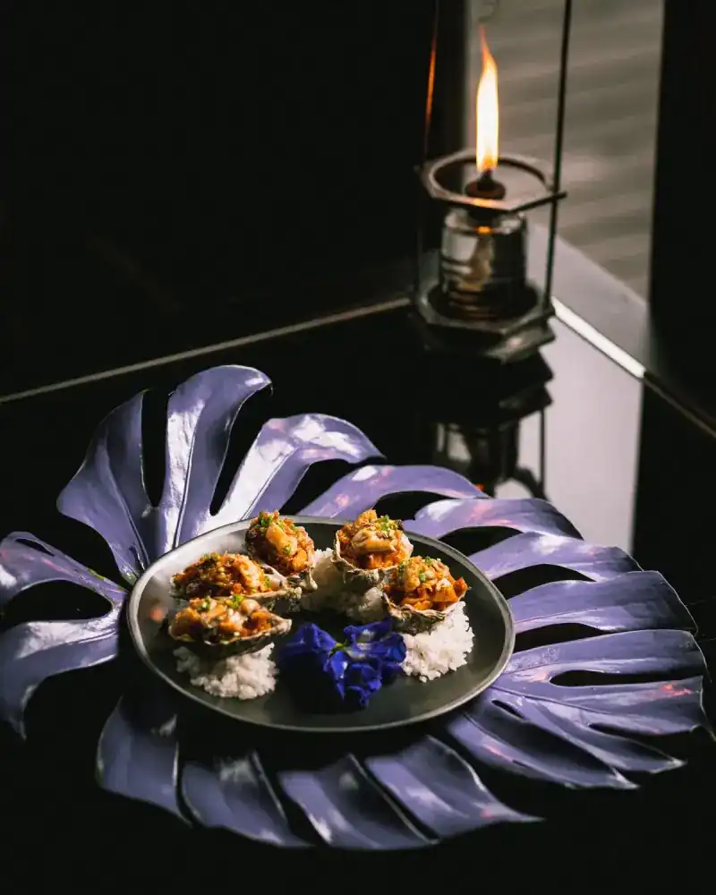 Shellfish on rice with blue flowers, served on a lilac leaf-shaped plate by candlelight