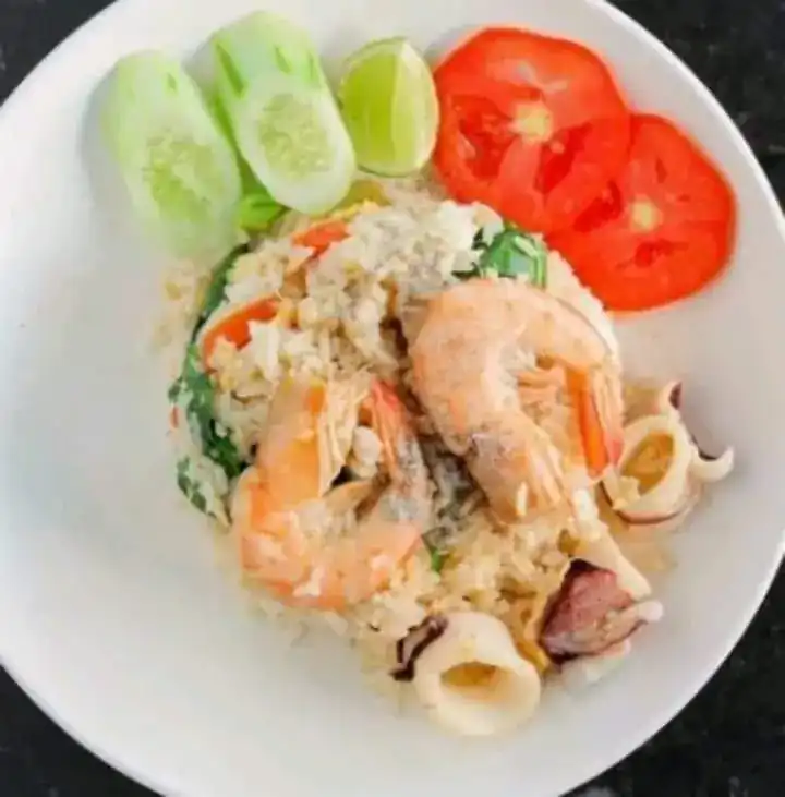 Seafood fried rice with prawns and squid, cucumber, lime and tomato on a white plate