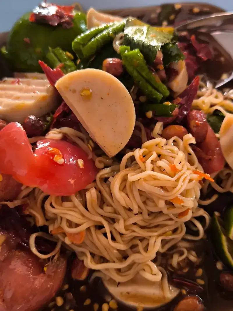 Close-up of a spicy tam with noodles, sliced pork sausage, tomato and long beans