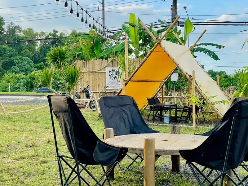 Black camping chairs around a round wooden table on the grass, a canvas tent behind