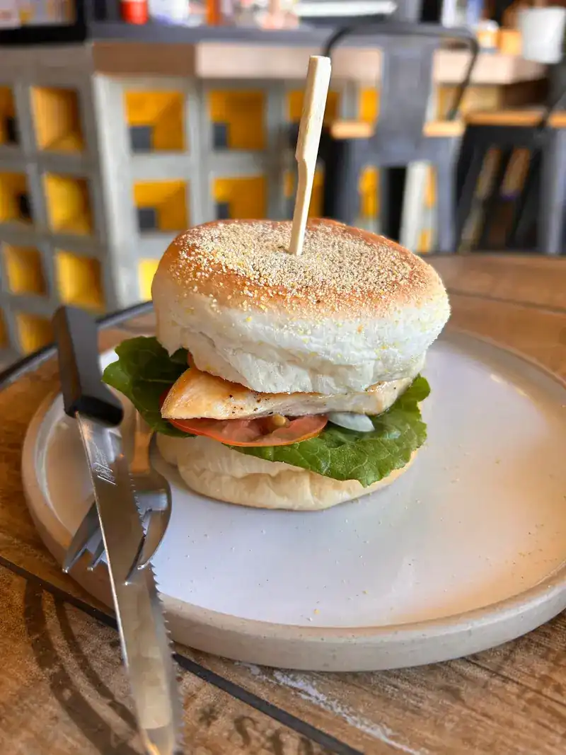 A burger on a sesame bun with lettuce and tomato, yellow block wall behind