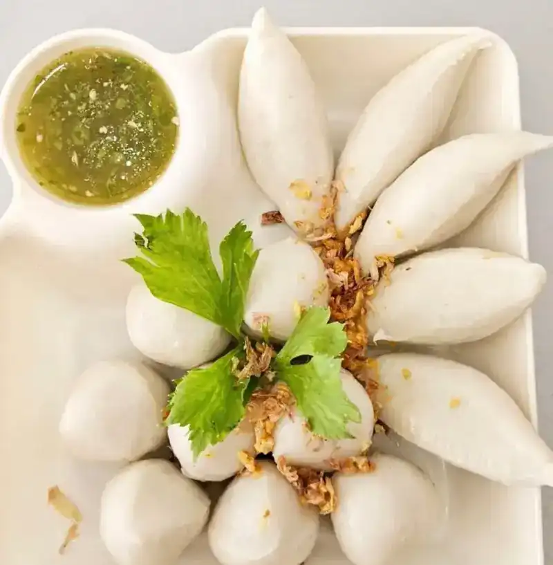 Fish dumplings and white balls arranged on a plate, with a green dipping sauce
