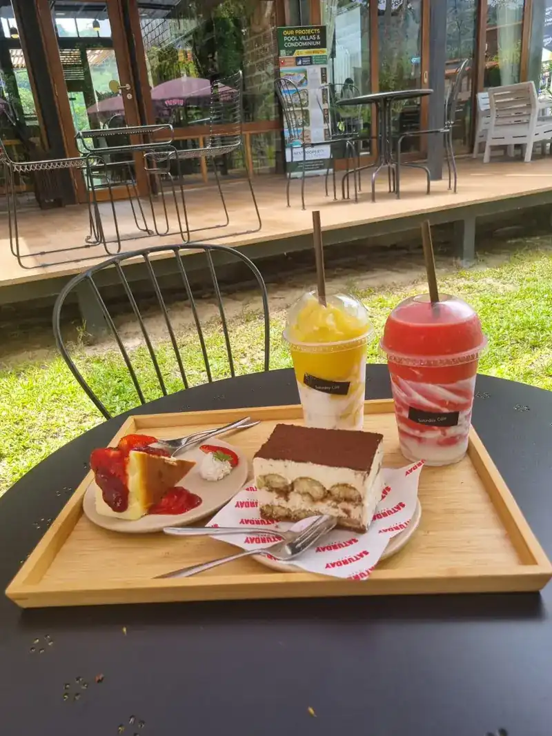 Tiramisu, a strawberry cake and two iced drinks on a tray, at a table on the lawn
