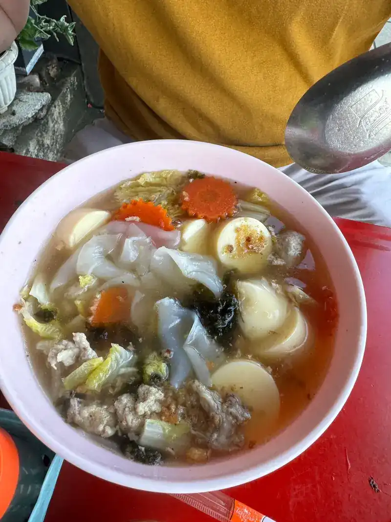 A bowl of clear soup with egg tofu, minced pork, seaweed, carrot and cabbage