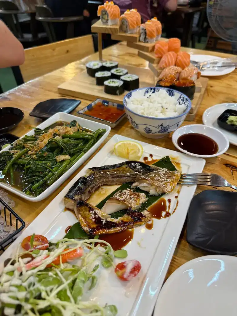 Stir-fried morning glory, grilled fish and rice, with sushi on wooden stands behind