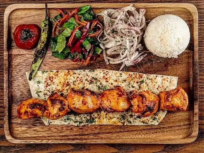 Grilled chicken on flatbread with roasted tomato, green chilli, onion salad and rice on a wooden board. ไก่ย่างบนแผ่นแป้ง พร้อมมะเขือเทศย่าง พริกย่าง สลัดหอมใหญ่ และข้าว บนถาดไม้