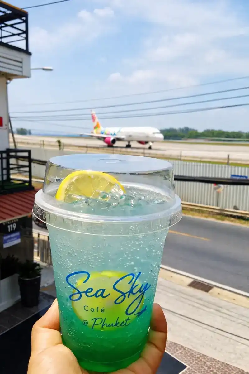 An iced blue soda in a Sea Sky cup, with a plane on the runway behind