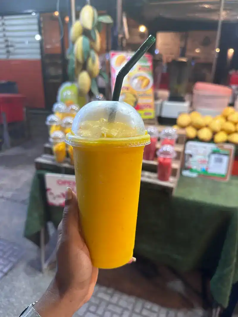 A hand holding a cup of thick mango drink in front of the stall
