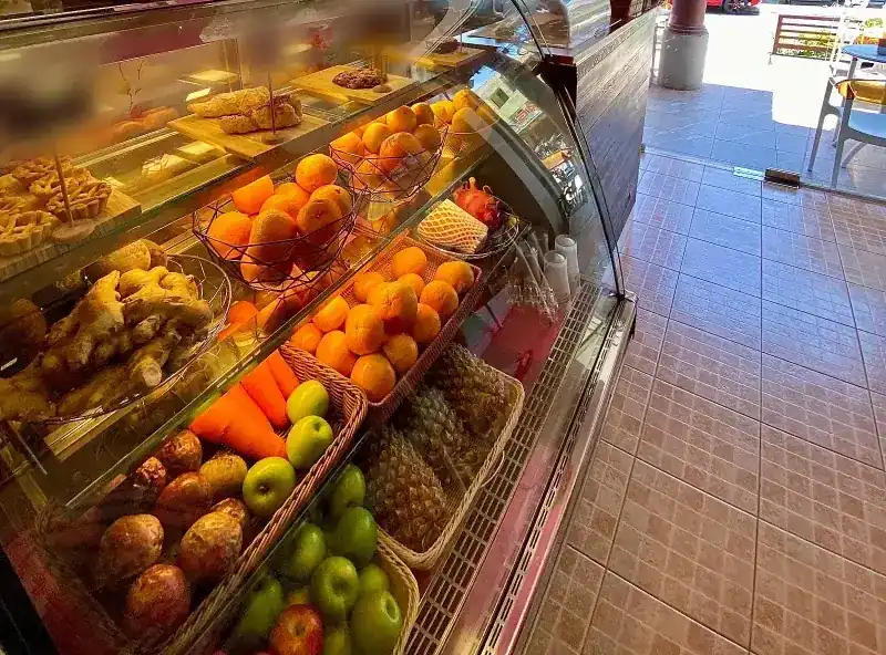 Glass counter with pastries on the top shelf and baskets of oranges, apples and pineapples below