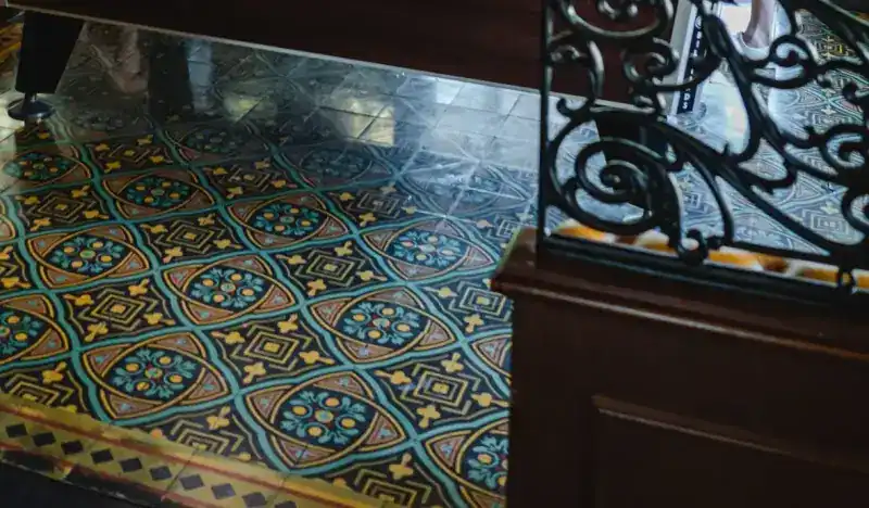 Patterned floor tiles in teal and mustard beside a wrought-iron screen and dark wood panelling