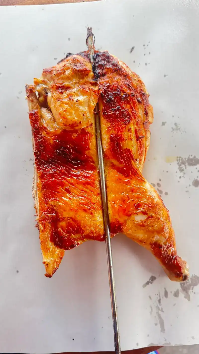 A whole grilled chicken, opened flat on a skewer, laid on paper