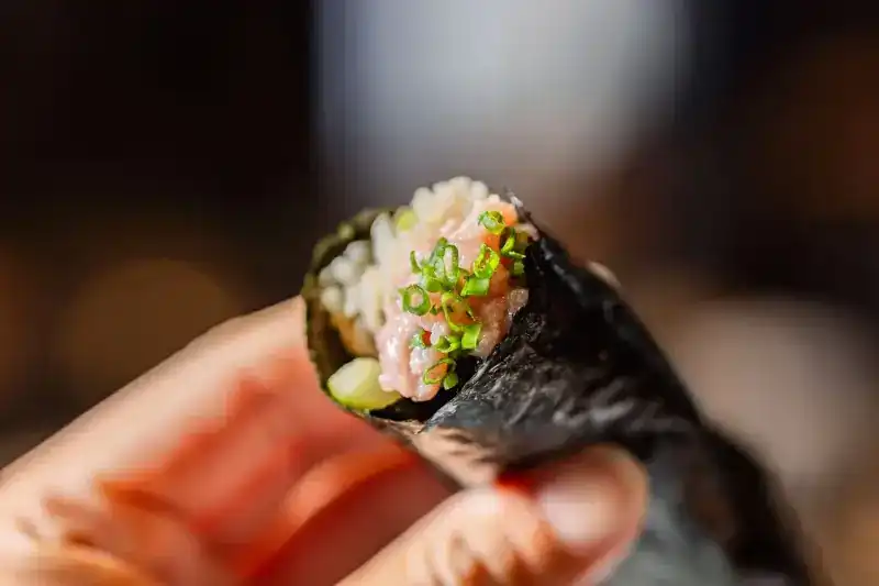 A tuna and spring onion hand roll held up close