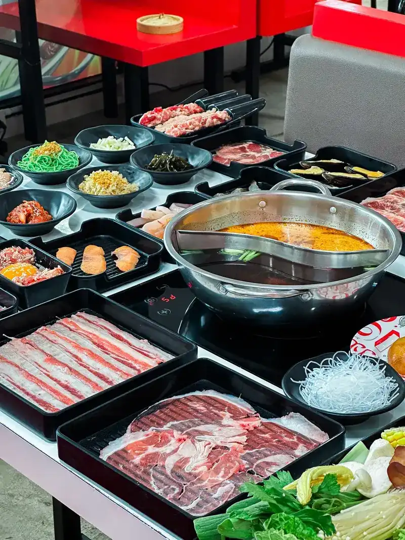 Trays of sliced beef, greens and glass noodles around a divided hot pot