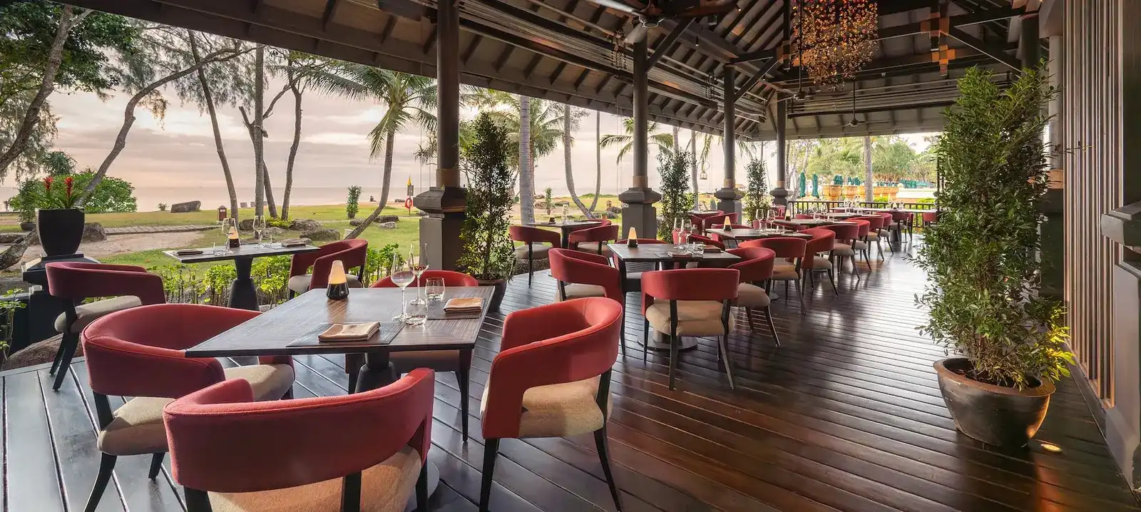The open-air dining deck with red armchairs, palm trees and the sea beyond