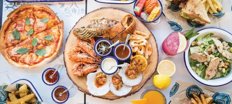 A wooden board of grilled prawns, scallops, lobster and calamari with pizza, salad and fries around it