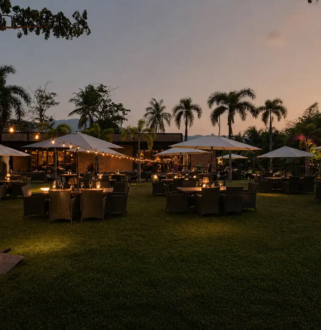 The garden at dusk: tables under white umbrellas and strings of lights, palms against a pink sky